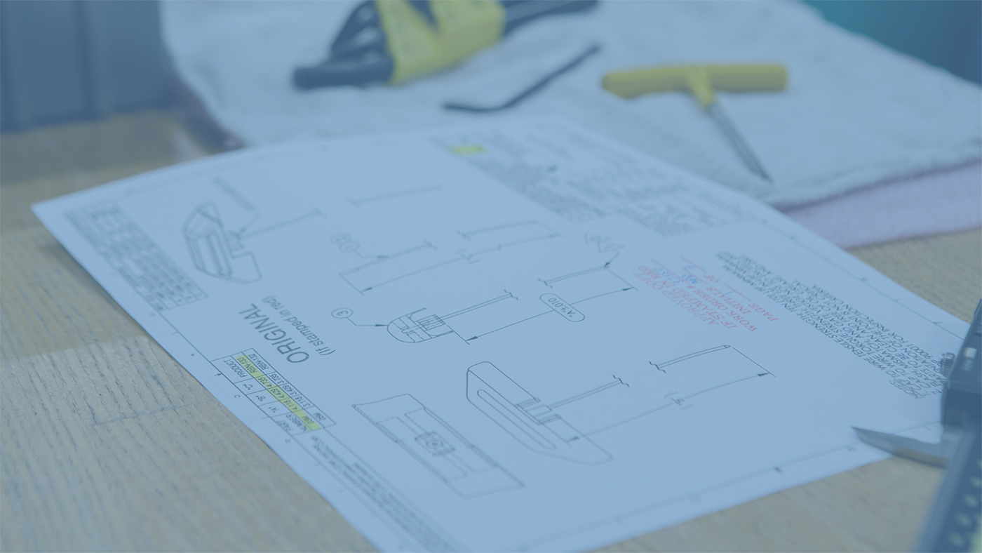 Pieces of paper with diagrams and notes for a medical device manufacturing project lying on a desk in a workshop